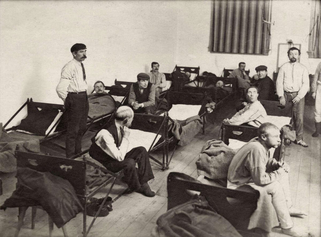 Mannen maken zich op om naar bed te gaan op de slaapzaal van het tehuis, aldus het tijdschrift Het Leven in een reportage over het Buitengasthuis van Hulp voor Onbehuisden in 1911