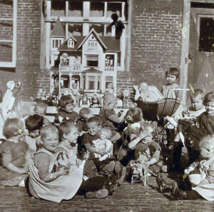 Kinderen spelen met een poppenhuis op de binnenplaats van het Oud Buitengasthuis van HvO in 1928
