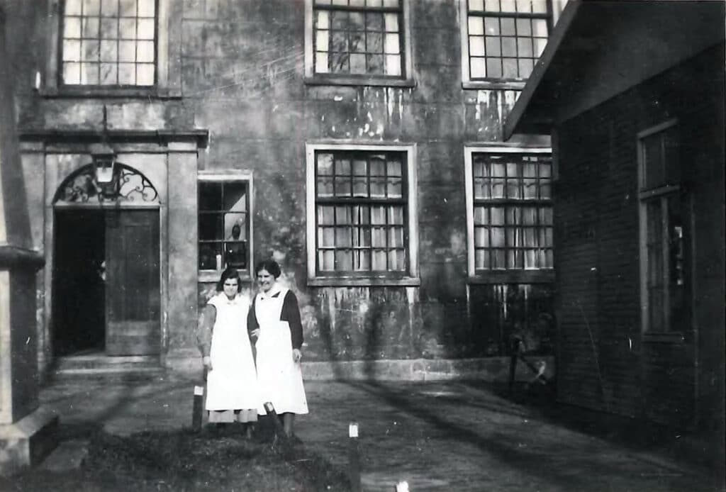 Twee medewerkers, Carla Hohn en zuster Van Doorn, voor het Oud Buitengasthuis van Hulp voor Onbehuisden in 1936. Links is nog net de rand van het monumentje voor de Jonkers te zien.