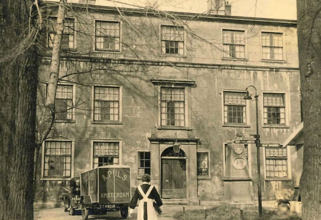 De voorgevel van het Oud Buitengasthuis van HvO in de jaren dertig met op de voorgrond een zuster, het monument voor de Jonkers en een verhuisauto van firma Puls die in de oorlog berucht zou worden