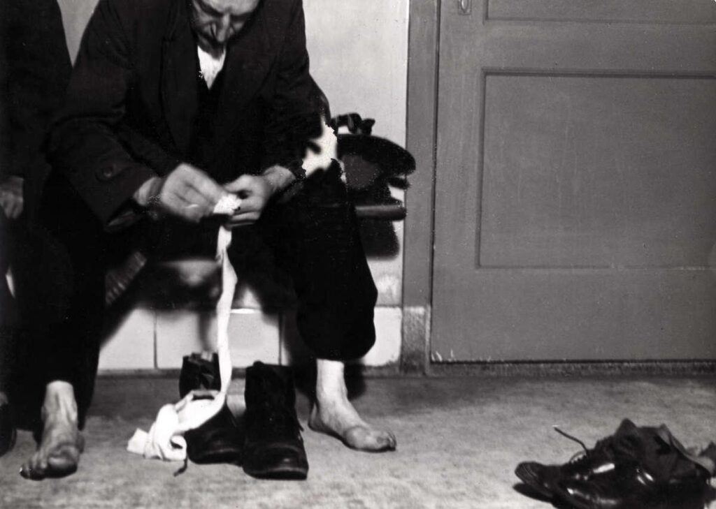 Nachtasiel van vereniging voor onbehuisden Amsterdam. Man met ontblote voeten bezig met zwachtel in het asiel, foto uit Het Leven, 1939