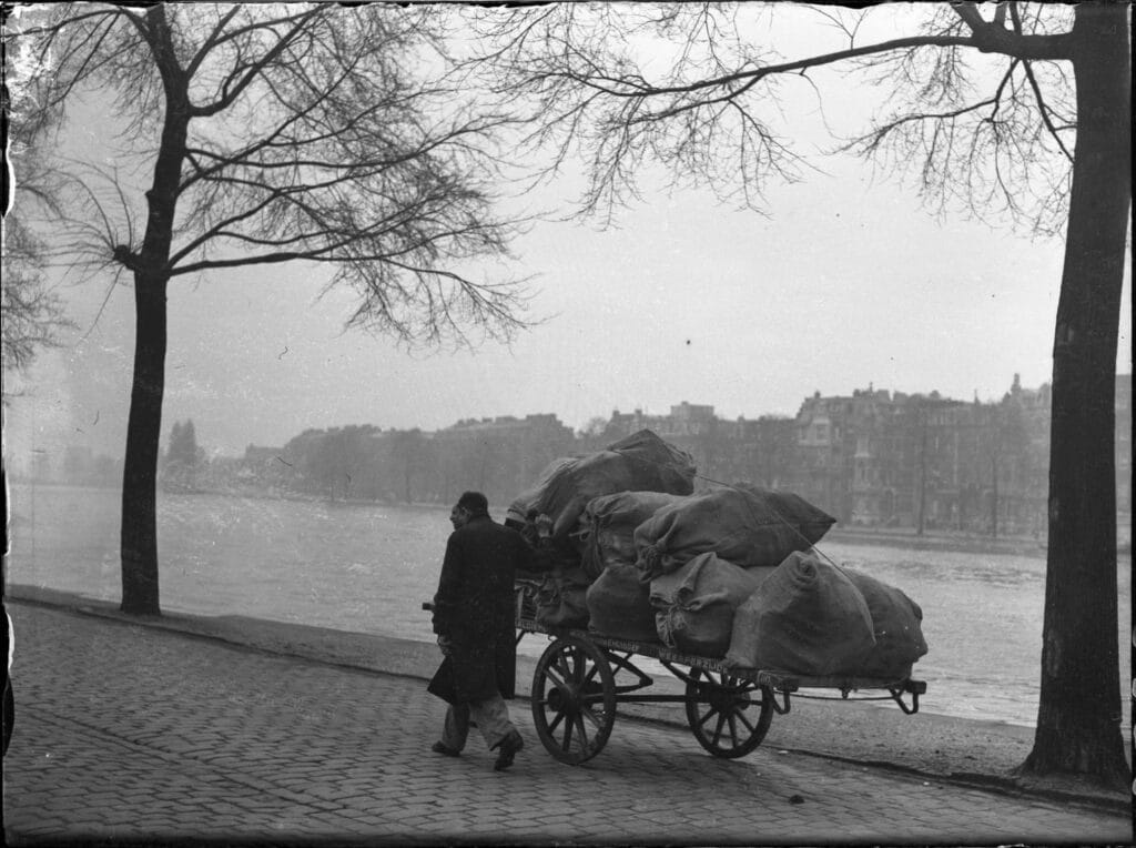 Twee mannen met een, met oud papier volgeladen, handkar van de materiaaldienst van de Hulp voor Onbehuisden, Weesperzijde, Amsterdam, 18 november 1947, Foto Ben van Meerendonk, collectie IISG.