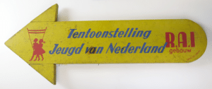 Wim-Brusse-Bewegwijzeringsbord-bij-tentoonstelling-Jeugd-van-Nederland-in-RAI-–gebouw-aan-Ferdinand-Bolstraat-19-augustus-18-september-1949