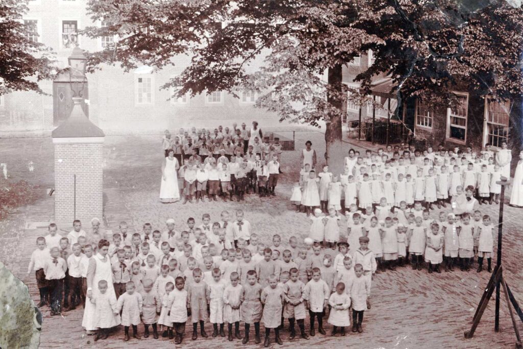 Kinderen en begeleiders op de binnenplaats van het Oud Buitengasthuis van Hulp voor Onbehuisden in 1908