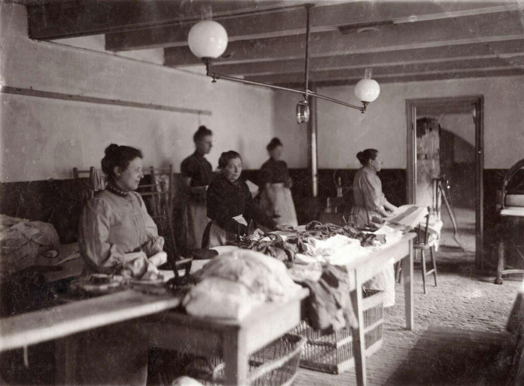 Vrouwen aan het werk op een werkplaats in het tehuis, aldus het tijdschrift Het Leven in een reportage over het Buitengasthuis van Hulp voor Onbehuisden in 1911