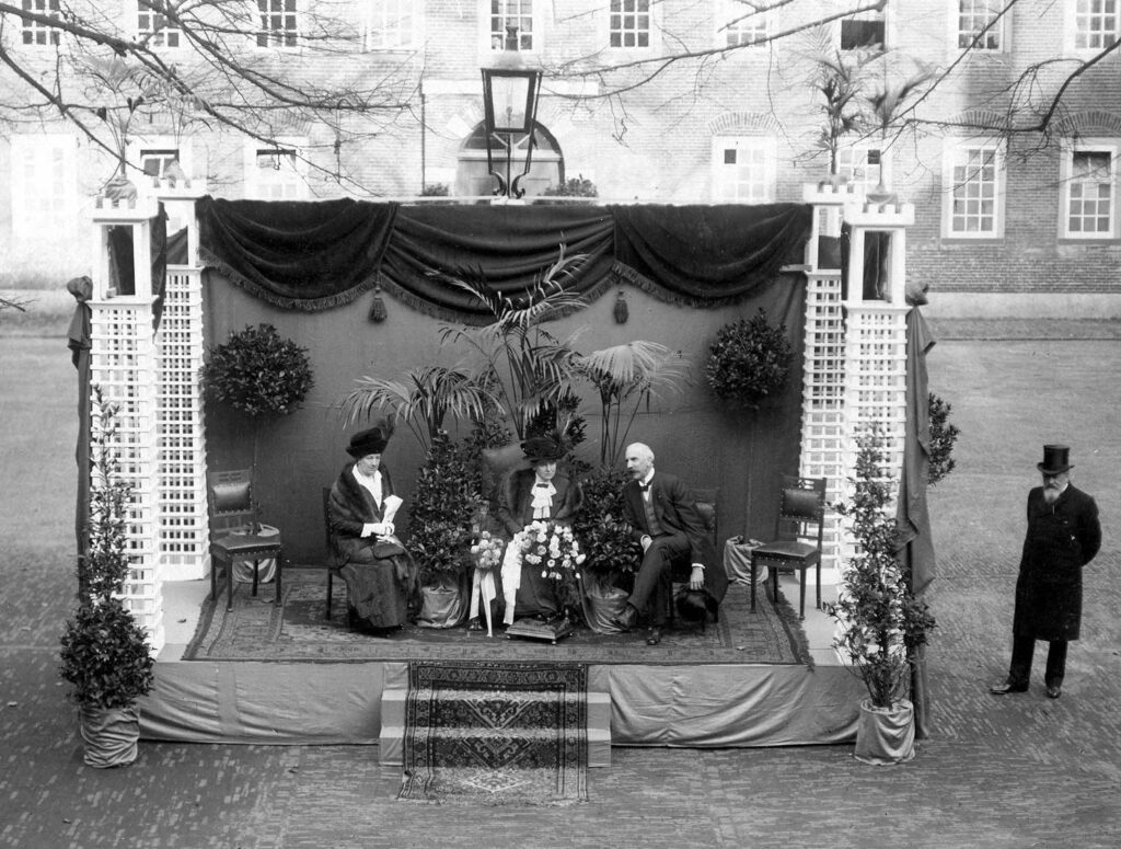 Koningin Wilhelmina op bezoek bij Hulp voor Onbehuisden, 24 oktober 1913. De koningin wordt geflankeerd door mevrouw Van Loon-Egidius, hofdame, en mr. J.G. Schölvinck, bestuurslid van HvO, foto Willy Zimmerman