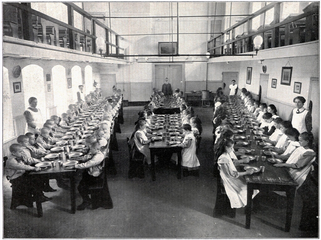 Eetzaal voor kinderen in het Oud Buitengasthuis van HvO in 1915. Midden achter de tafel staat Jonker.