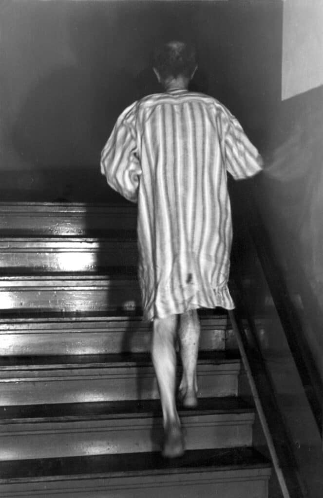 Nachtasiel van HvO. Man in nachthemd wandelt een trap op in het asiel, foto uit Het Leven, 1939